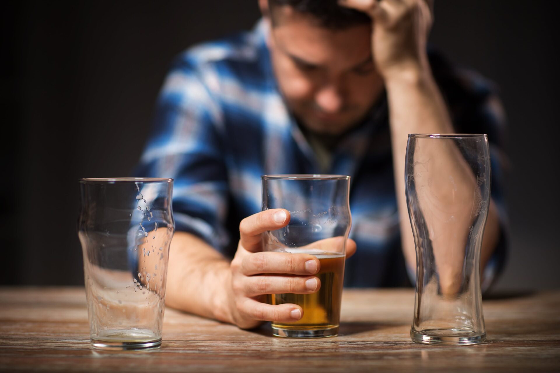 man with an alcohol addiction clutches a beer with head down