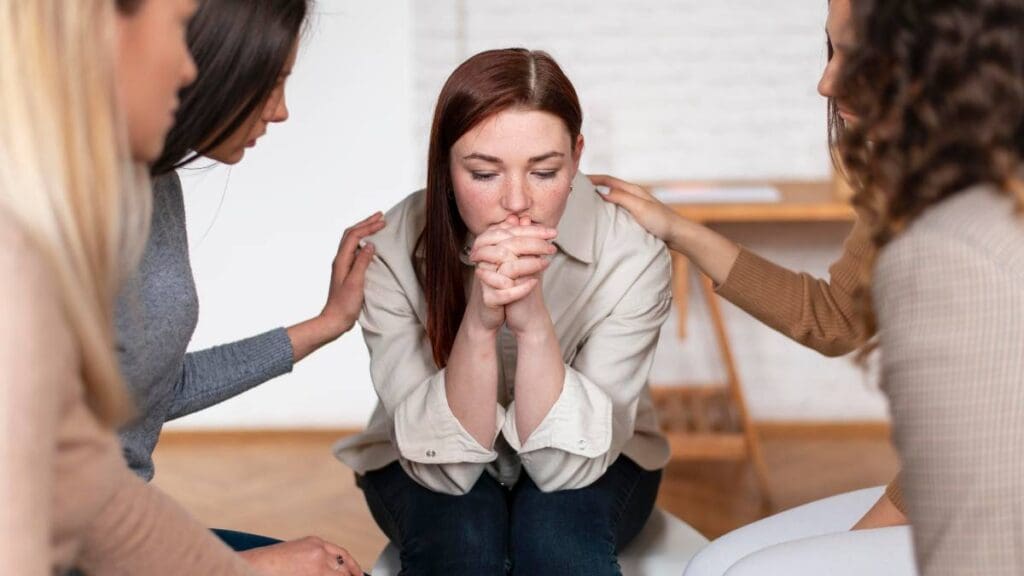 A young woman concerned about issues like "Can you get fired for going to rehab?", while receiving support from friends to begin treatment. 